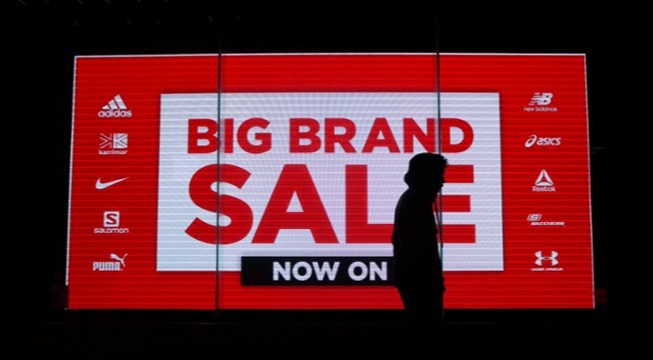 dark silhouette walking past big brand sale sign