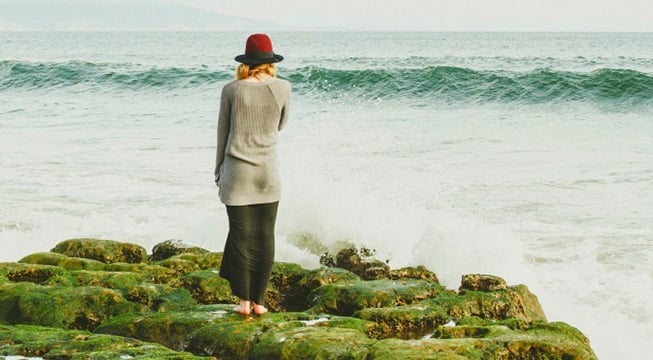 woman standing on large mossy rocks in front of body of water